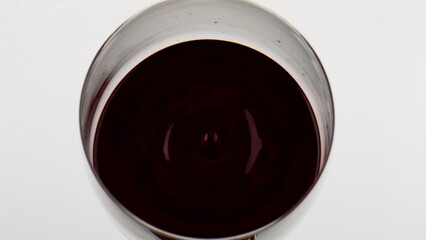 Red wine droplet falling rippling in goblet closeup. Smooth beverage surface