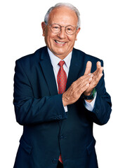 Senior man with grey hair wearing business suit and glasses clapping and applauding happy and joyful, smiling proud hands together - obrazy, fototapety, plakaty