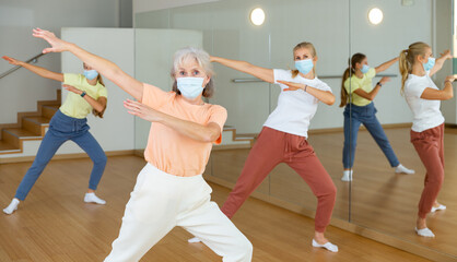 Obraz premium Elderly woman in face mask learning aerobic dance with her younger relatives in studio.