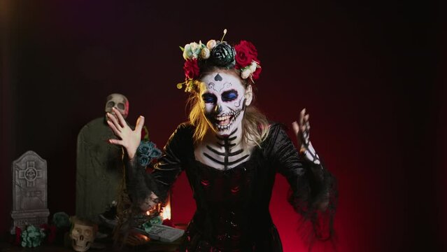 Horror goddess of death yelling in costume with skull body art, wearing flowers crown and screaming like holy santa muerte to celebrate dios de los muertos. Woman on tranditional mexican holiday.