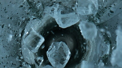 Ice cubes falling blender closeup. Grinding iced pieces in container top view.
