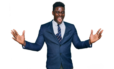 Handsome business black man wearing business suit and tie celebrating mad and crazy for success with arms raised and closed eyes screaming excited. winner concept