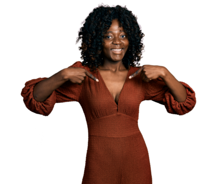 African woman with curly hair wearing casual dress looking confident with smile on face, pointing oneself with fingers proud and happy.