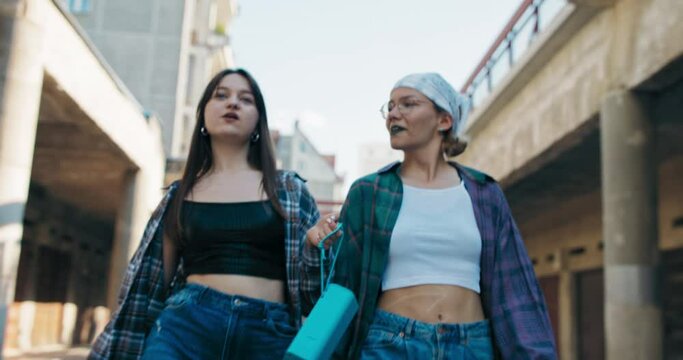Two teenagers walk along the street dressed in loose clothes revealing the girls' athletic bellies. In hand, a portable speaker connected wirelessly to a phone that turns on music thanks to an app.