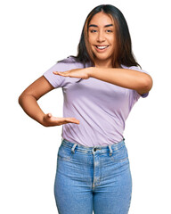 Obraz premium Young latin woman wearing casual clothes gesturing with hands showing big and large size sign, measure symbol. smiling looking at the camera. measuring concept.