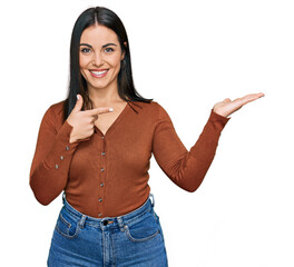 Young hispanic woman wearing casual clothes amazed and smiling to the camera while presenting with...