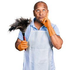 Hispanic middle age man wearing apron holding cleaning duster serious face thinking about question...