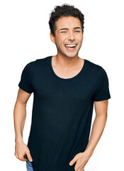 Young handsome man wearing casual black t shirt winking looking at the camera with sexy expression, cheerful and happy face.