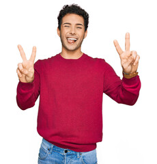 Young handsome man wearing casual clothes smiling with tongue out showing fingers of both hands doing victory sign. number two.