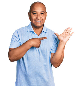 Hispanic middle age man wearing casual t shirt amazed and smiling to the camera while presenting with hand and pointing with finger.