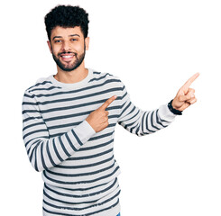 Naklejka premium Young arab man with beard wearing casual striped sweater smiling and looking at the camera pointing with two hands and fingers to the side.