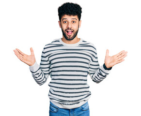 Young arab man with beard wearing casual striped sweater celebrating crazy and amazed for success with arms raised and open eyes screaming excited. winner concept