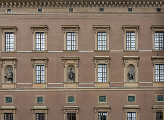Fototapeta na wymiar Sweden, Stockholm - July 16, 2022: Royal Palace. SW Slottsbacken facade closeup with rectangular windows and 3 male statues in niches