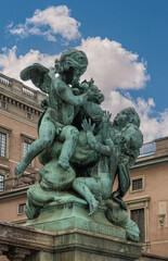 Sweden, Stockholm - July 16, 2022: Royal Palace. Green bronze Mercy statue at edge of Logarden along Skeppsbron under blue cloudscape. Beige east facade as backdrop