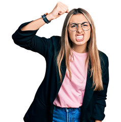 Hispanic young woman wearing business jacket and glasses angry and mad raising fist frustrated and...