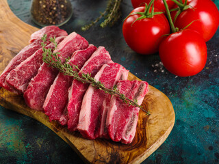 Close-up. Homemade raw beef steaks with a sprig of rosemary on a wooden cutting board and ripe red tomatoes on a marble dark background. Restaurant, hotel, home cooking.