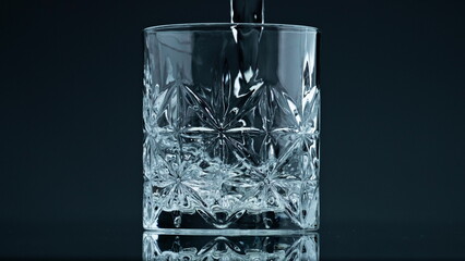 Crystal water pouring glass at dark background closeup. Fresh liquid splashing