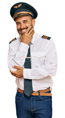 Handsome man with beard wearing airplane pilot uniform looking confident at the camera smiling with crossed arms and hand raised on chin. thinking positive.
