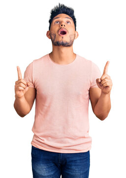 Handsome latin american young man wearing casual clothes amazed and surprised looking up and pointing with fingers and raised arms.