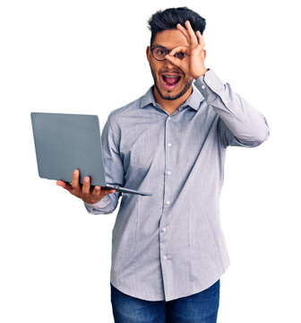 Handsome latin american young man working using computer laptop smiling happy doing ok sign with hand on eye looking through fingers