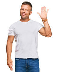 Handsome muscle man wearing casual white tshirt showing and pointing up with fingers number five while smiling confident and happy.