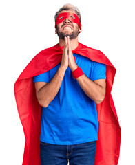 Young blond man wearing super hero custome begging and praying with hands together with hope expression on face very emotional and worried. begging.