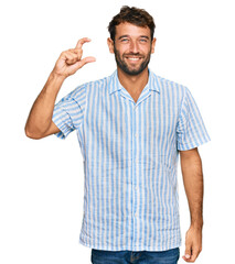 Naklejka premium Handsome young man with beard wearing casual fresh shirt smiling and confident gesturing with hand doing small size sign with fingers looking and the camera. measure concept.