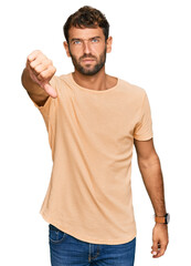 Naklejka premium Handsome young man with beard wearing casual tshirt looking unhappy and angry showing rejection and negative with thumbs down gesture. bad expression.