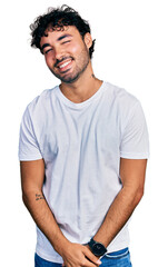 Hispanic young man with beard wearing casual white t shirt winking looking at the camera with sexy expression, cheerful and happy face.
