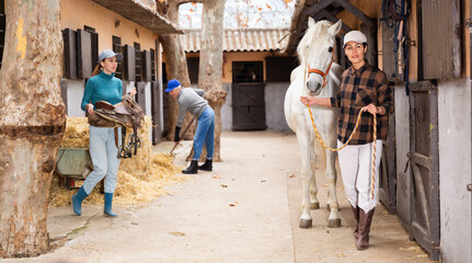 Group of female workers of stable doing daily chores in yard on autumn day, Asian woman leading...