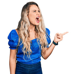 Young blonde woman pointing with fingers to the side angry and mad screaming frustrated and furious, shouting with anger. rage and aggressive concept. - obrazy, fototapety, plakaty