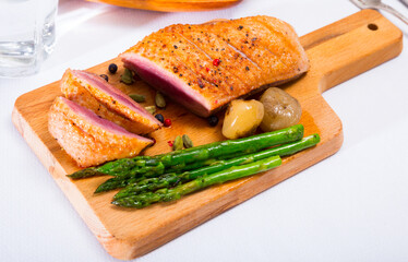 Tasty roasted duck breast with asparagus and herbs served on cutting board