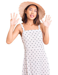 Young beautiful chinese girl wearing summer hat showing and pointing up with fingers number nine while smiling confident and happy.