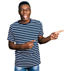 Young african american man pointing with fingers to the side sticking tongue out happy with funny expression.