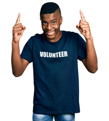 Young african american man wearing volunteer t shirt smiling amazed and surprised and pointing up with fingers and raised arms.