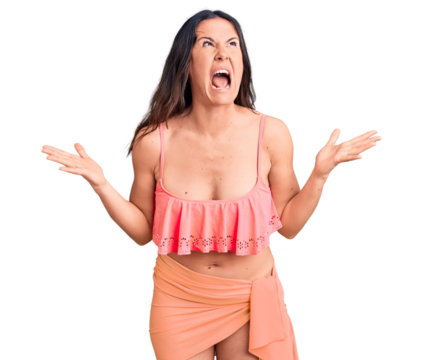 Young beautiful brunette woman wearing bikini crazy and mad shouting and yelling with aggressive expression and arms raised. frustration concept.