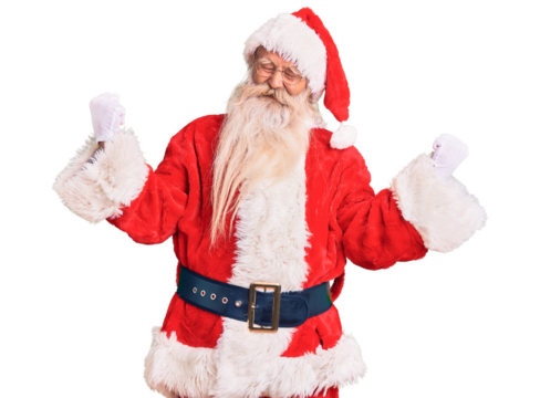 Old senior man with grey hair and long beard wearing traditional santa claus costume very happy and excited doing winner gesture with arms raised, smiling and screaming for success. celebration