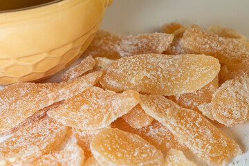 Close up view of crystallized ginger next to a yellow bowl with honeycomb pattern.