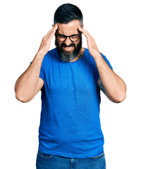 Fototapeta premium Hispanic man with beard wearing casual t shirt and glasses with hand on head for pain in head because stress. suffering migraine.