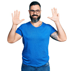 Hispanic man with beard wearing casual t shirt and glasses showing and pointing up with fingers number nine while smiling confident and happy.