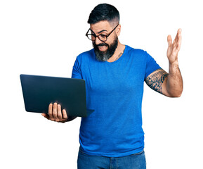 Hispanic man with beard working using computer laptop celebrating victory with happy smile and...
