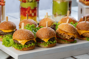 mini burgers with cheese and lettuce with sticks on a wooden background 