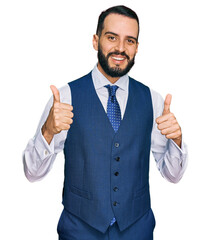 Young man with beard wearing business vest success sign doing positive gesture with hand, thumbs up smiling and happy. cheerful expression and winner gesture.