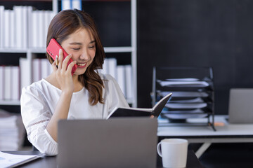 Young business asian woman cheerful Asian lady working at workplace office, workdesk with laptop financial documents having phone conversation, copy space