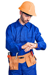 Young hispanic man wearing worker uniform checking the time on wrist watch, relaxed and confident