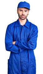 Young hispanic man wearing painter uniform skeptic and nervous, disapproving expression on face with crossed arms. negative person.