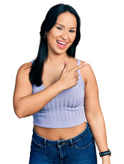 Fototapeta premium Beautiful hispanic woman wearing casual style with sleeveless shirt smiling cheerful pointing with hand and finger up to the side