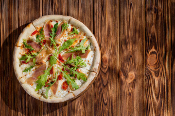 Pizza with jamon and prosciutto, mozzarella, cherry tomatoes, arugula and parmesan on a wood background. Italian cuisine.