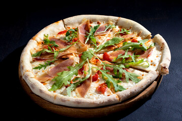 Pizza with jamon or prosciutto, mozzarella, cherry tomatoes, arugula and parmesan on a black background. Italian cuisine.