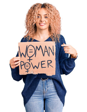 Young blonde woman with curly hair holding we need a change banner smiling happy pointing with hand and finger